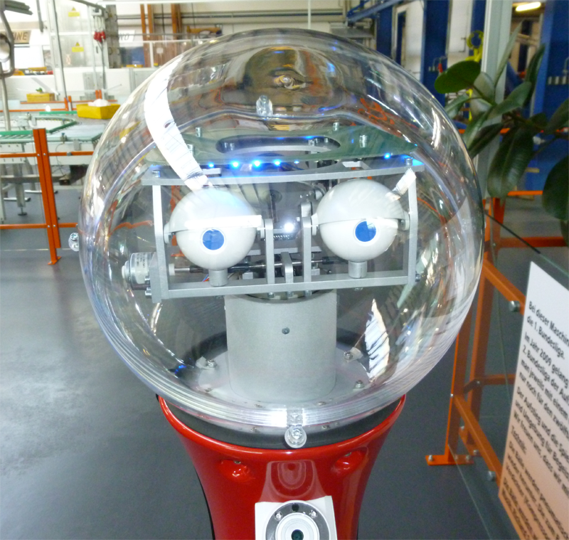 Roboter im Museum mit einer Glaskugel als Kopf und zwei Augen.