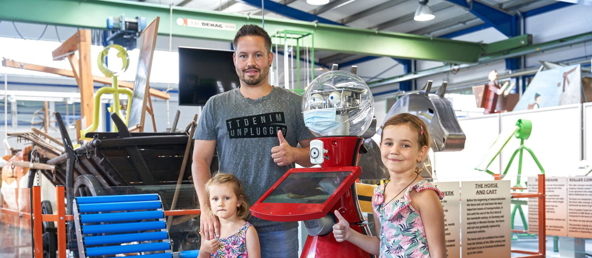 Vater mit zwei Töchtern neben einem roten Roboter.