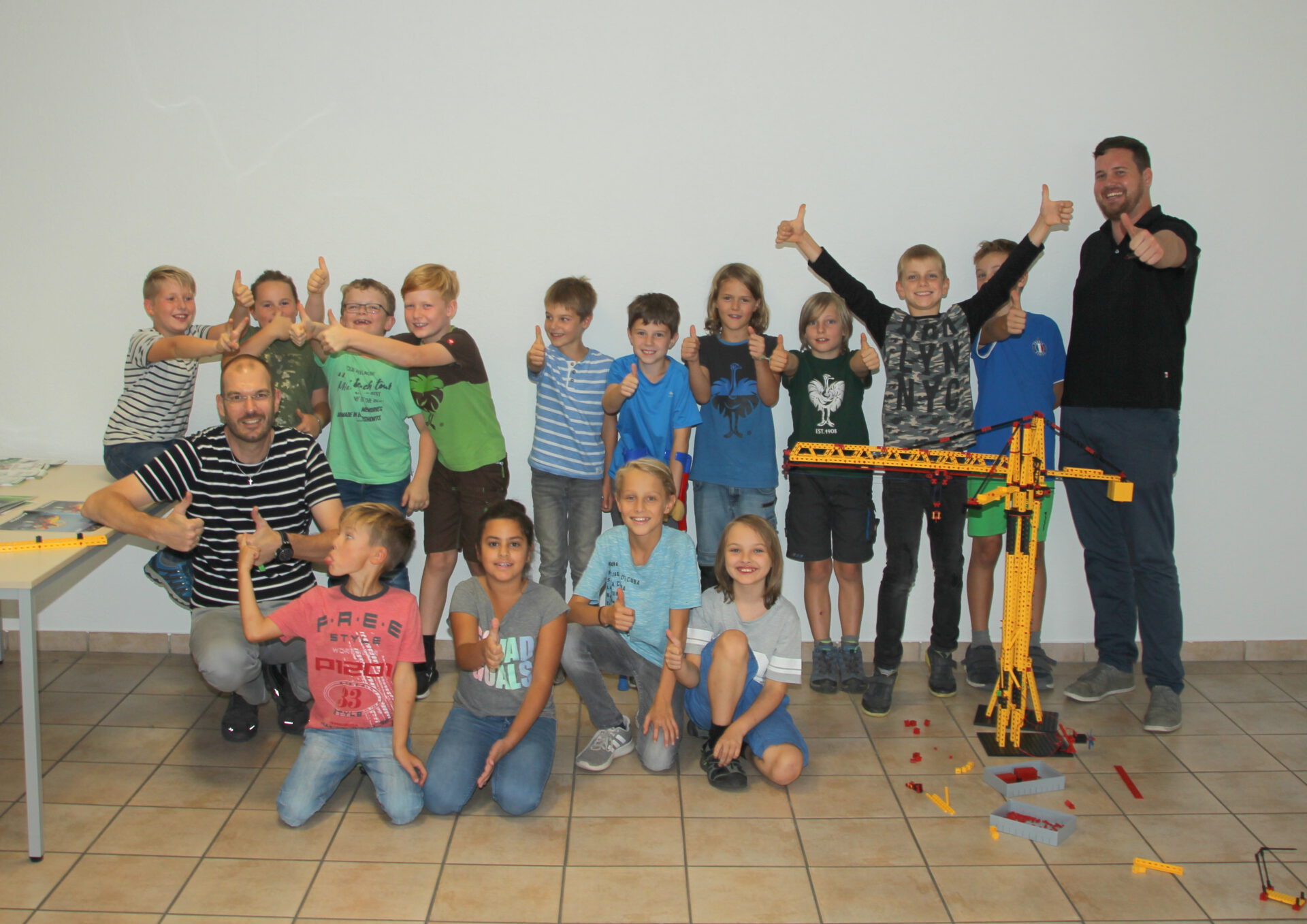 Lächelnde Gruppe von Kindern nach erfolgreichem Aufbau eines gelben Lego-Krans.